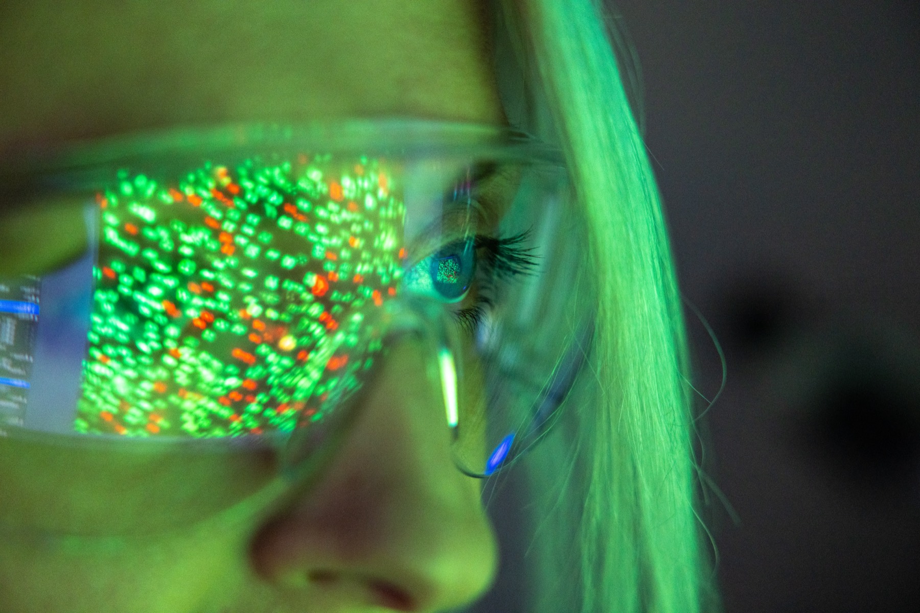 Fluorescent bacterial colonies reflected in a researcher's safety glasses